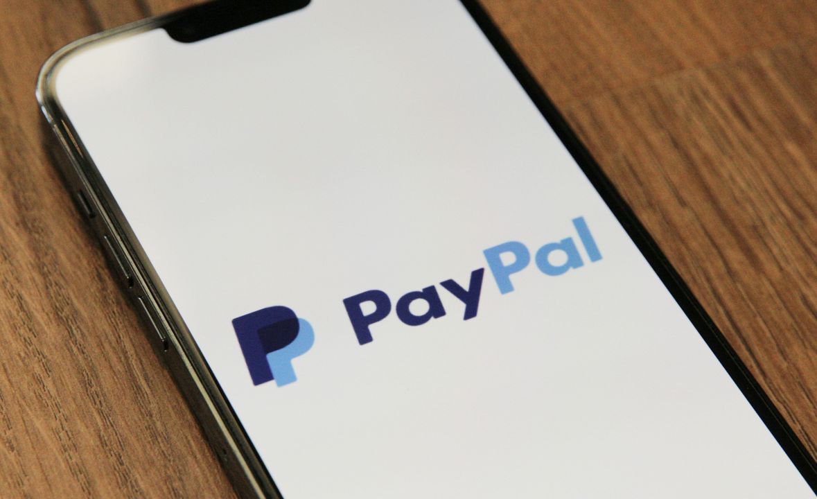 PayPal logo displayed on a smartphone screen resting on a wooden desk