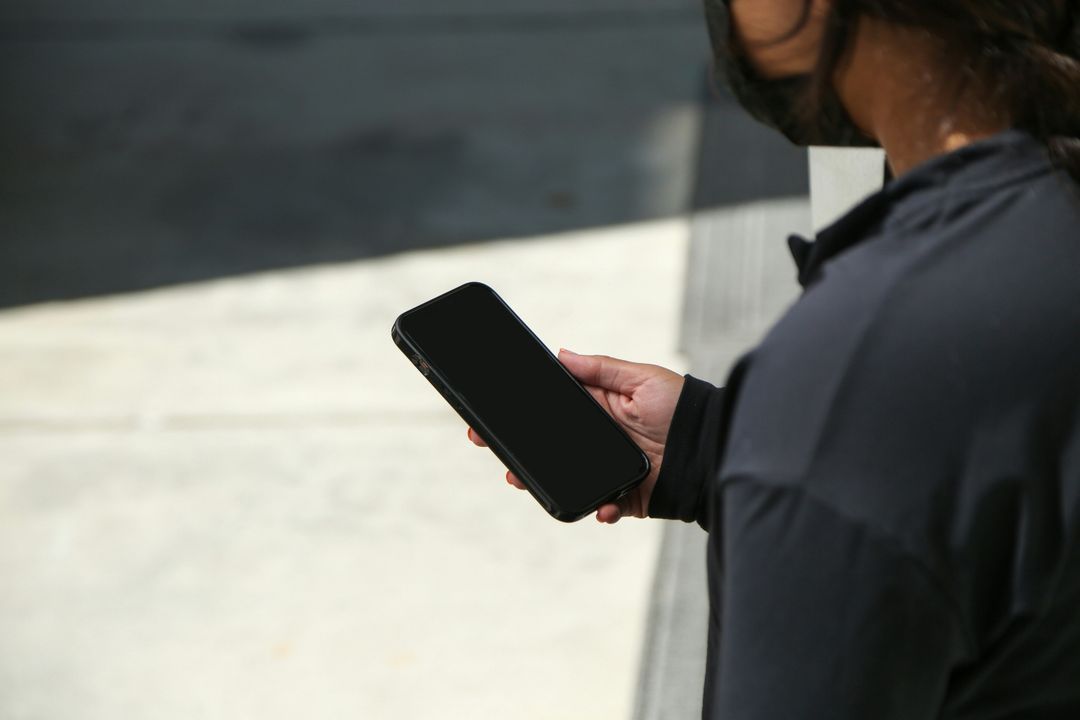 Person outdoors holding a smartphone with a blank screen