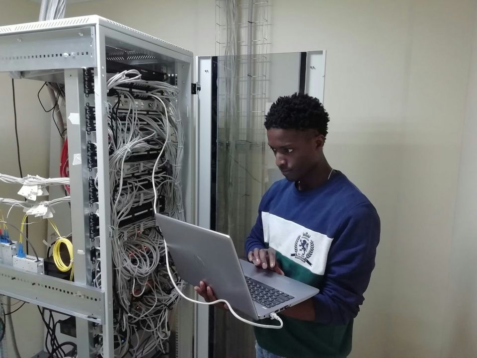 Person working on a laptop in front of an open network rack full of cabling