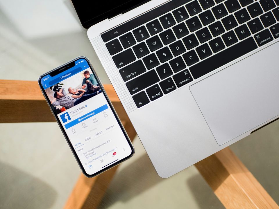 Phone showing the Facebook page resting beside a laptop keyboard