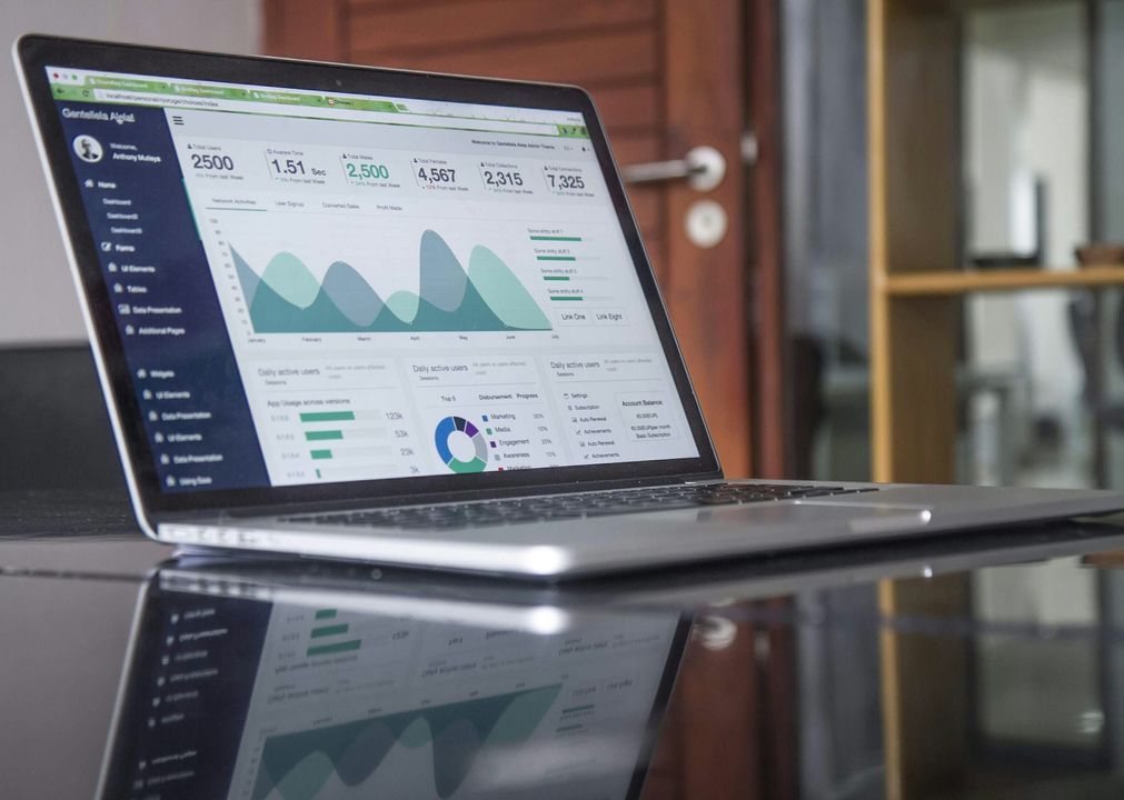 Laptop on a glass desk showing an analytics dashboard with user counts and trend charts