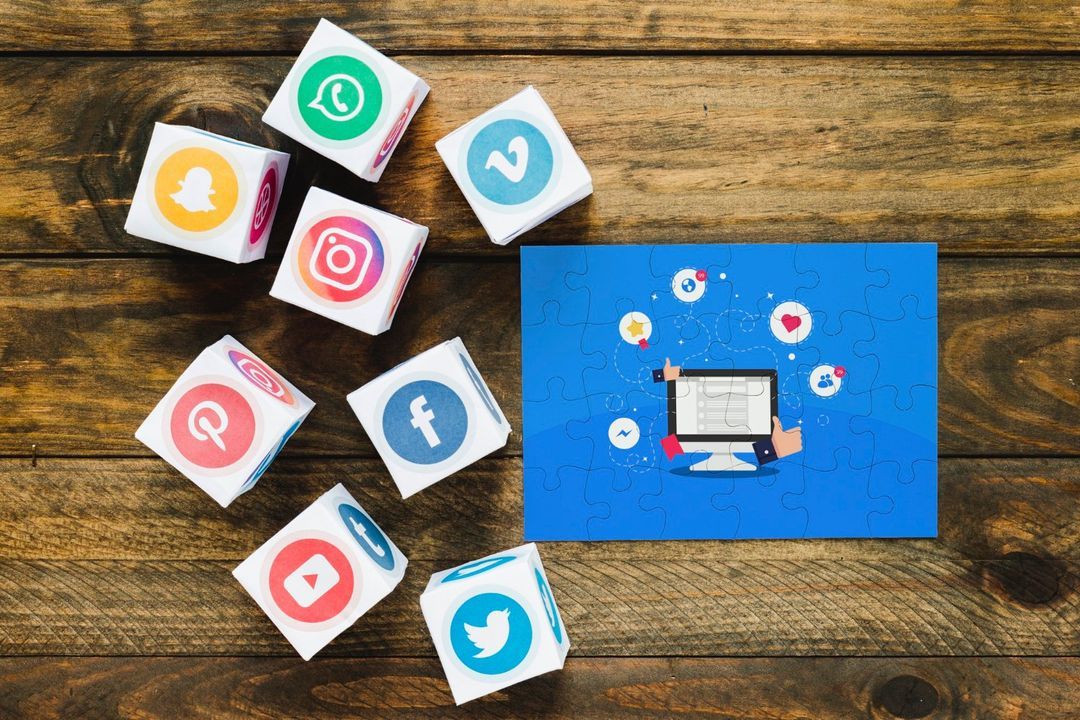 Cubes printed with social media logos on a wooden table beside a blue jigsaw illustration