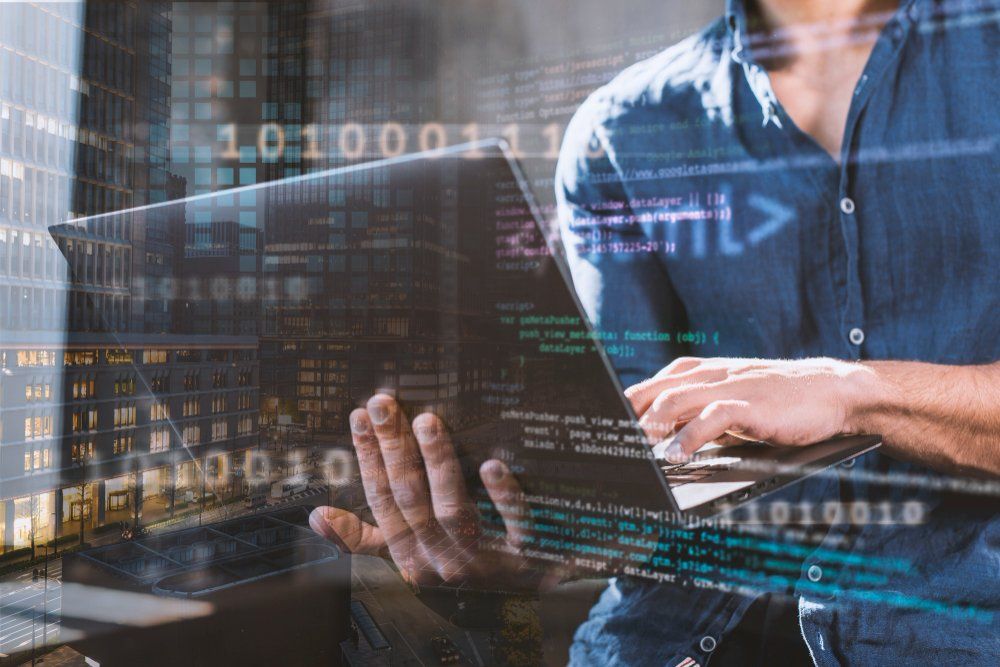 Double exposure of a person typing on a laptop over city buildings, binary digits and code